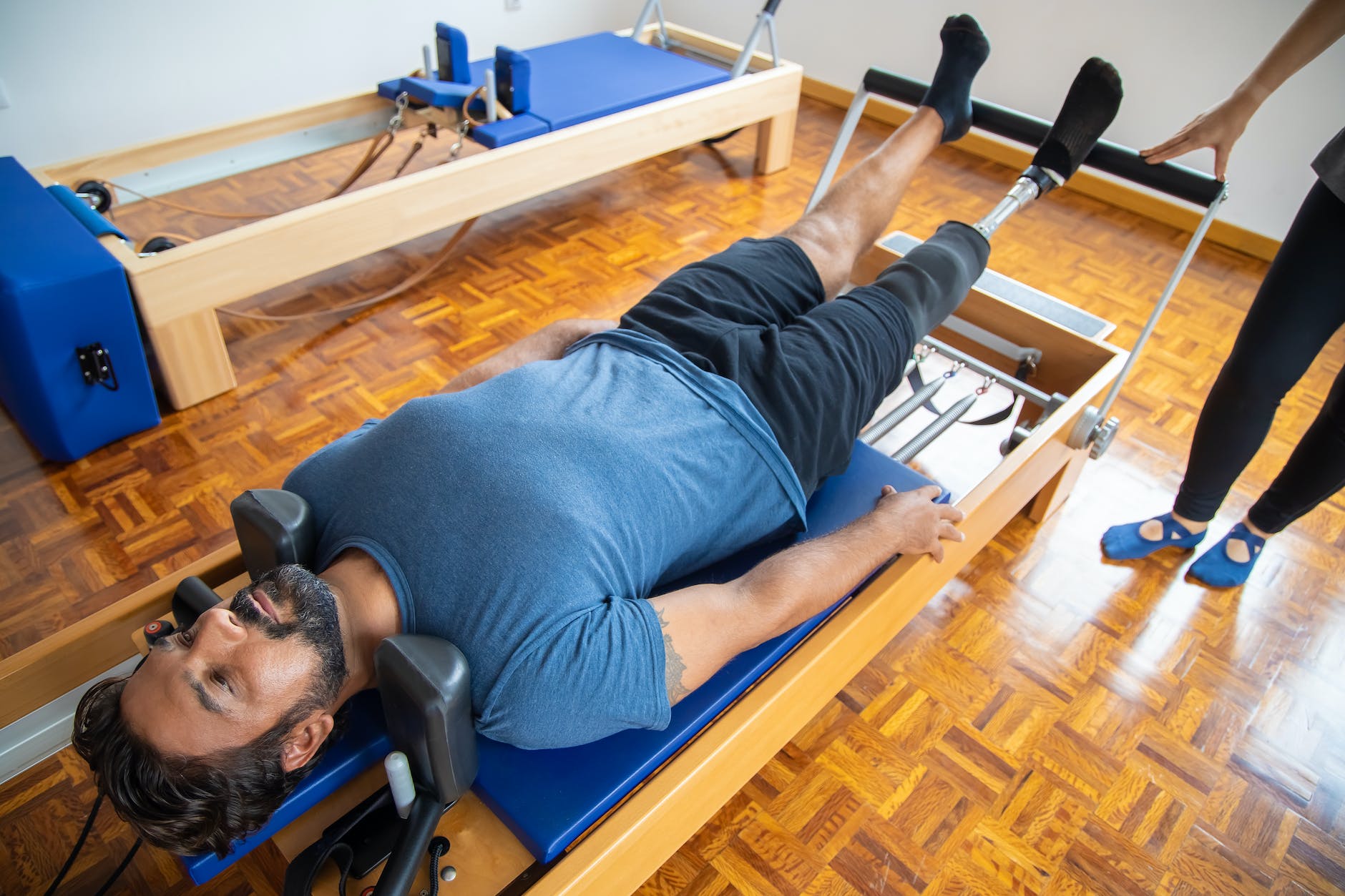 A man with a prosthetic leg is on a pilates reformer, which may be used in a physical therapy clinc.