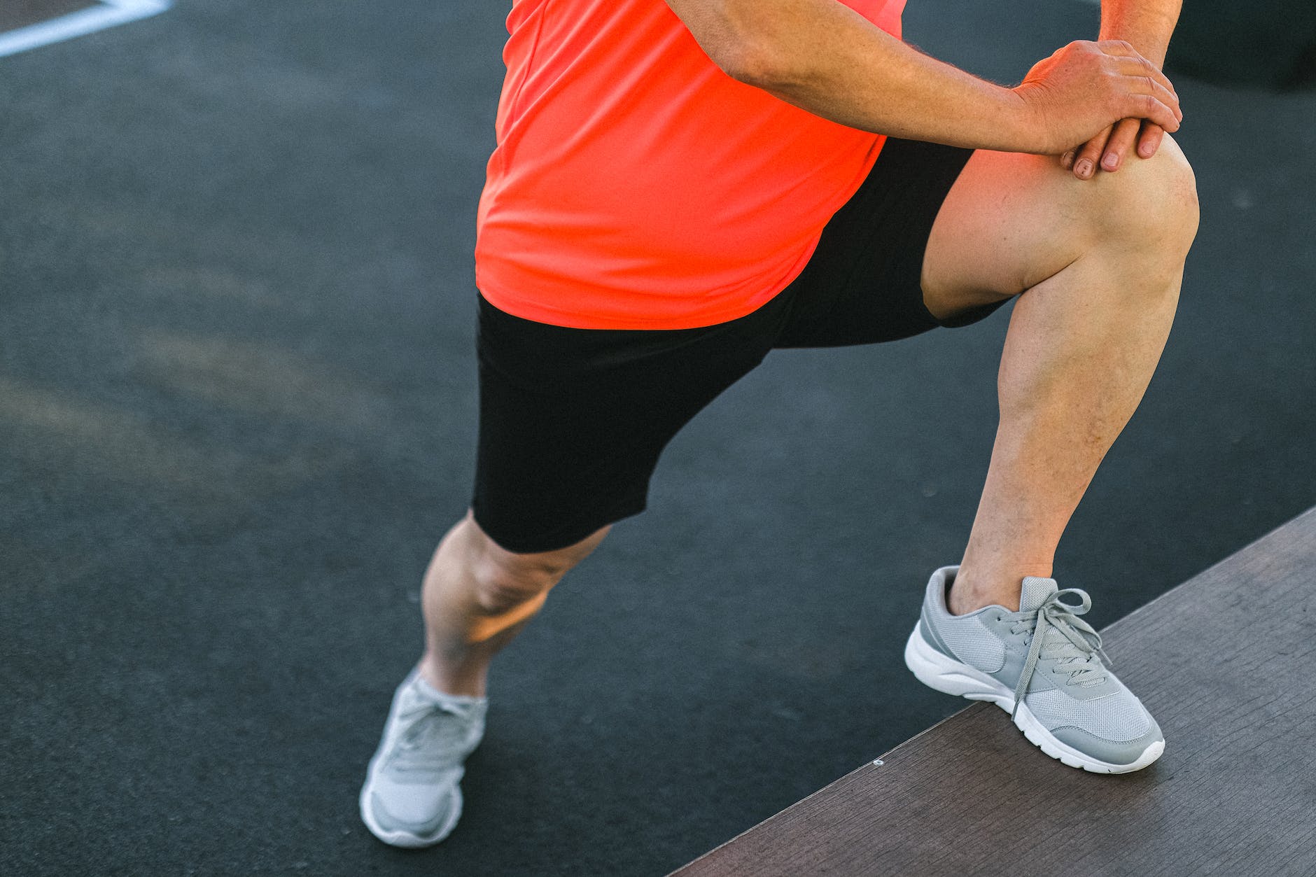 A runner stretches his calf in a standing position. He is also getting a stretch in the front of his hip because his front leg is elevated on a step.