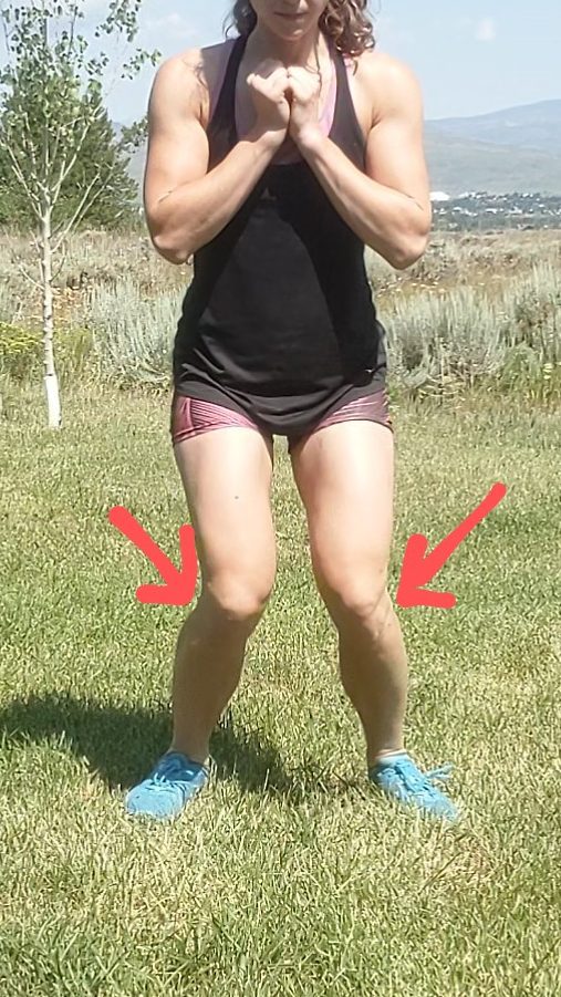 A partial depth squat, taken from the person facing the camera directly. Both knees are dipping to midline and there are arrows next to each knee showing the way they are falling in. This position usually causes medial knee pain. 