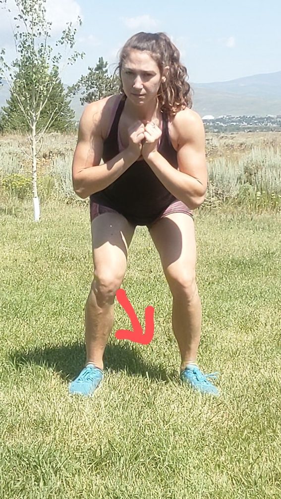 A squat with hips just above 90 the knees, taken from the person facing the camera directly. The person's right knee is dipping in towards midline, and there is an arrow indicating the direction the knee is tipping. Poor positioning can cause medial knee pain.