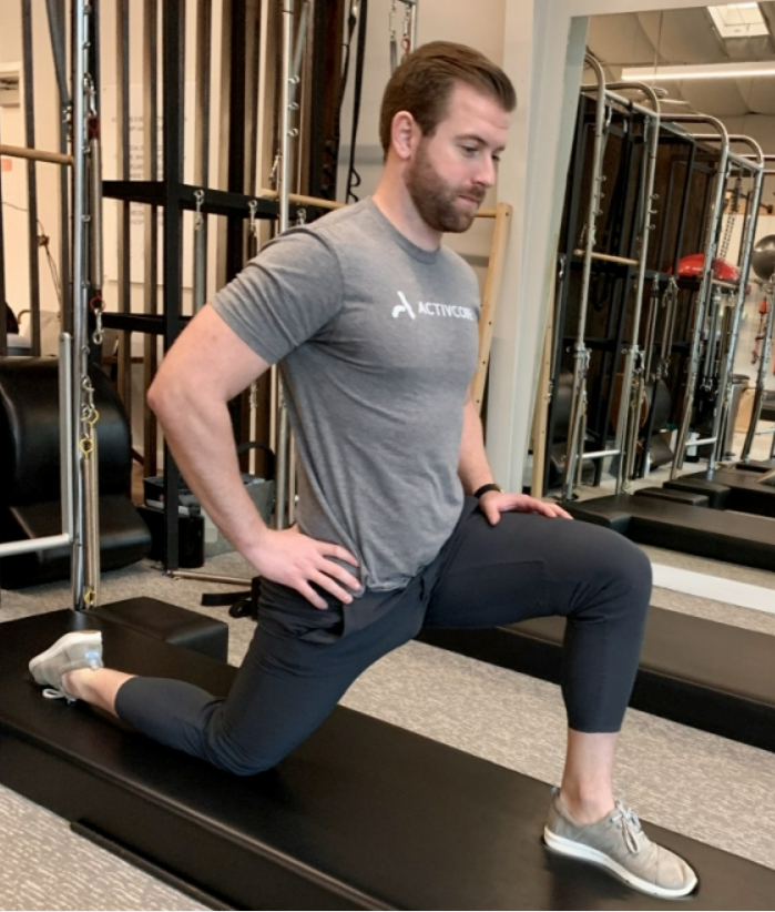 Lunging hip flexor stretch performed by a man on the floor, stretching the front of his right hip.