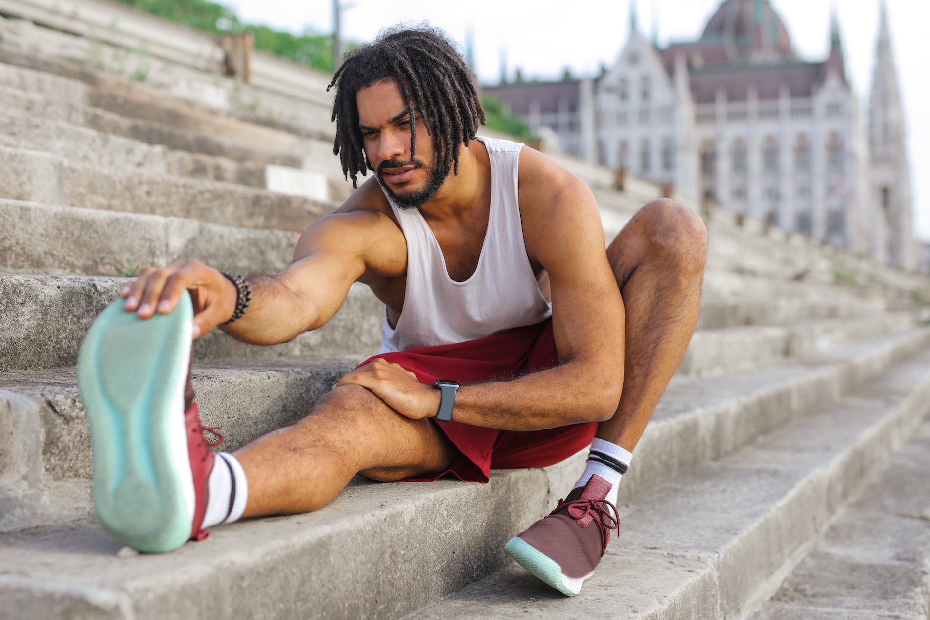 man in white tank top stretching on concrete stairs.